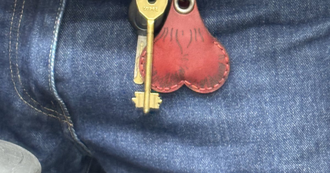 Red leather Lucky Pair AirTag holder and a brass key on denim jeans
