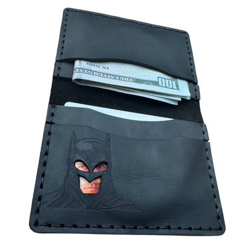 Open black leather bat bifold wallet with embossed superhero cowl and cutout eye window, holding cash and cards