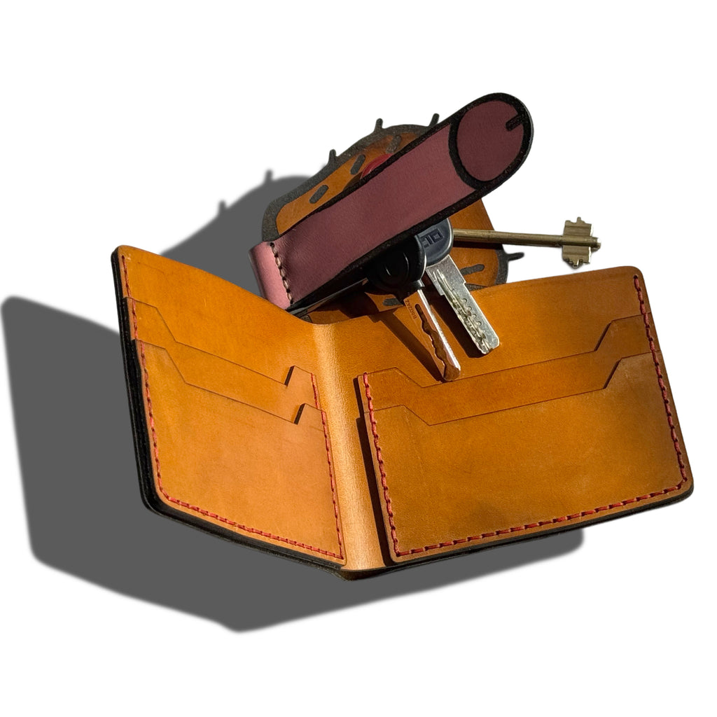 Interior view of a handmade leather bifold wallet with functional card slots, paired with a bold anatomical-style leather key holder securing metal keys. A functional and humorous adult novelty accessory set crafted from high-quality tan leather with red contrast stitching