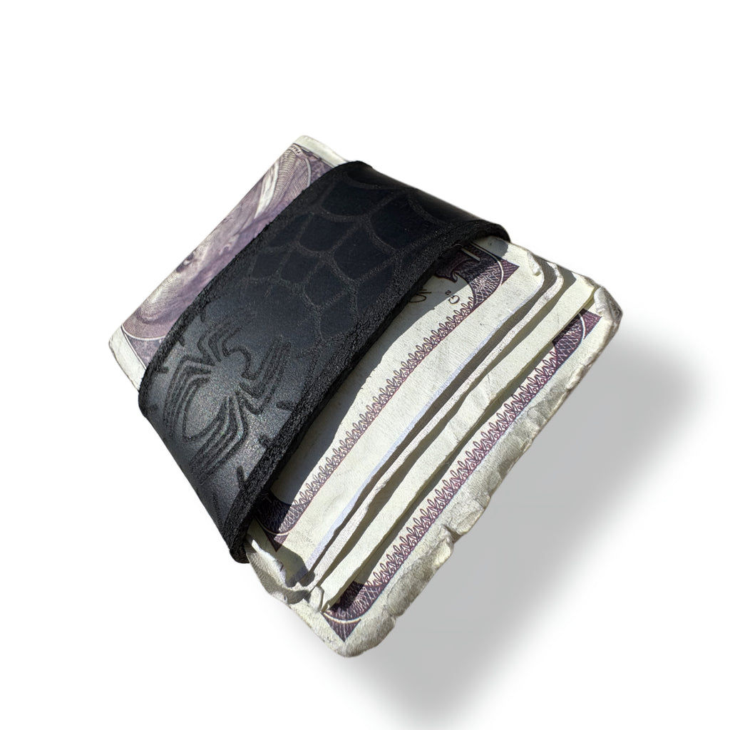 Black spider web leather money clip folded around a thick stack of banknotes