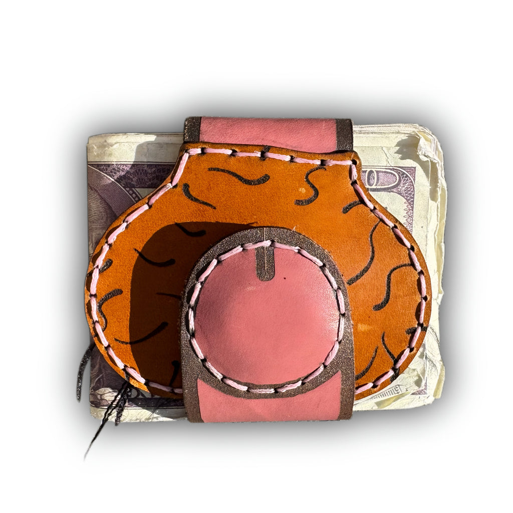 Au naturel leather money clip closed, round pink magnetic tip resting on the hair-tooled tan front over a stack of bills