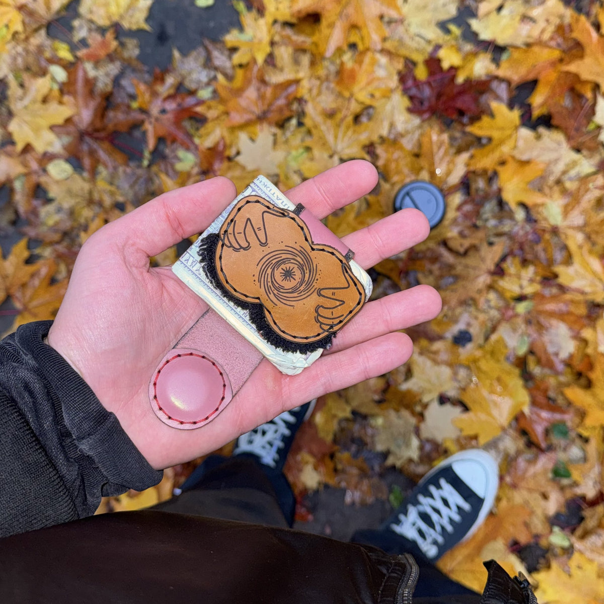 Black hole XL leather money clip closed over folded cash, held in an open palm