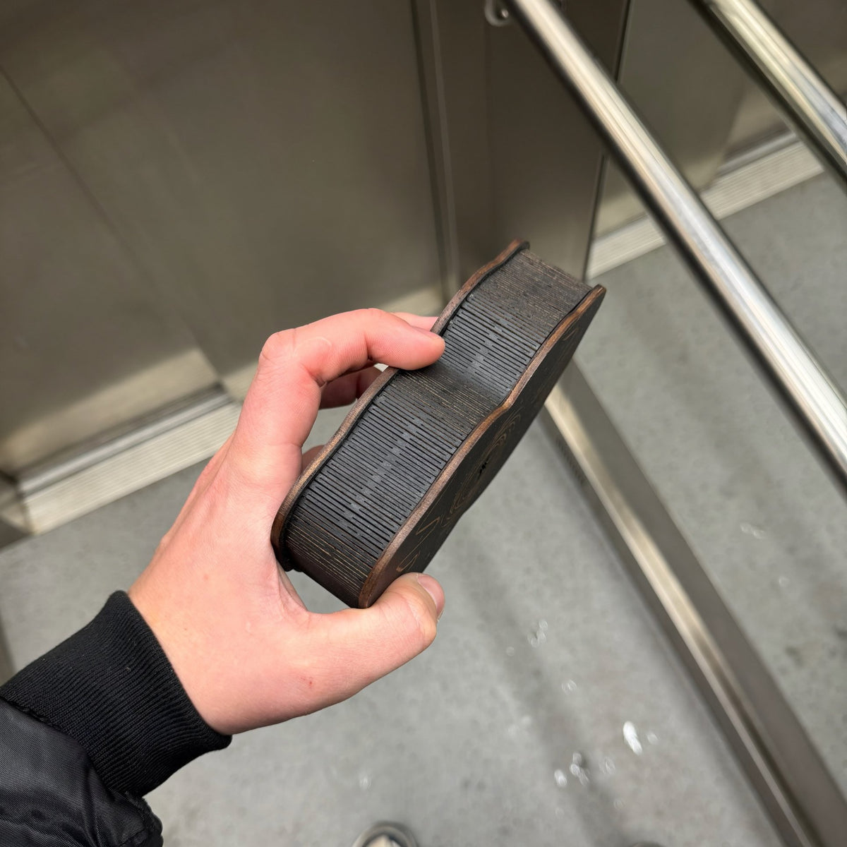 Side view of the black wooden gift box showing slatted bent wood walls in hand