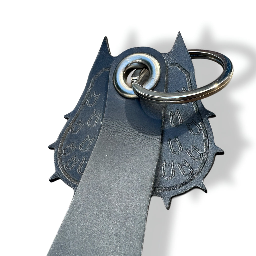 Close-up of pointed-ear cowl and engraved bat symbols on a black leather bat keychain