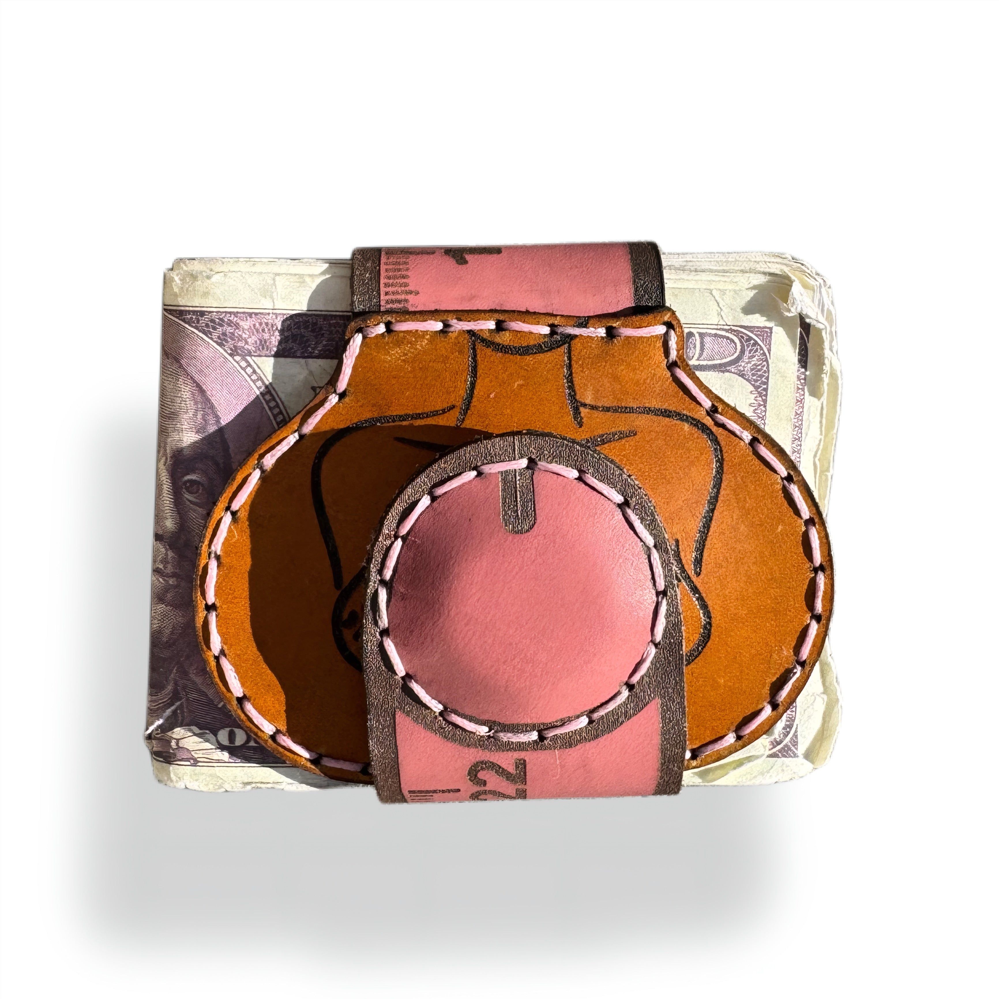 Ruler edition leather money clip closed, round pink magnetic tip pressed to the tan engraved front over folded banknotes