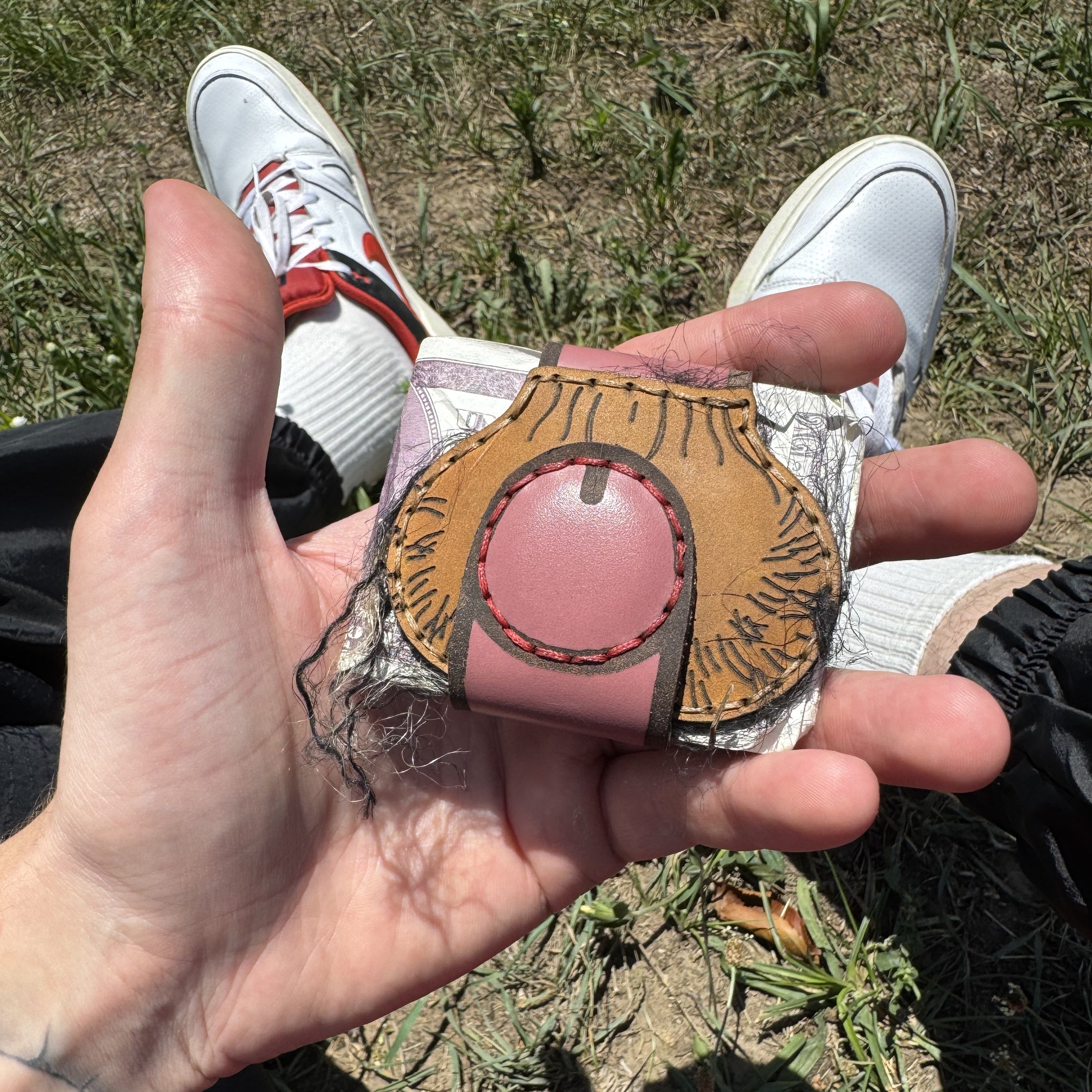 Tan leather XL cheeky money clip with a pink magnetic button, resting in an open palm outdoors